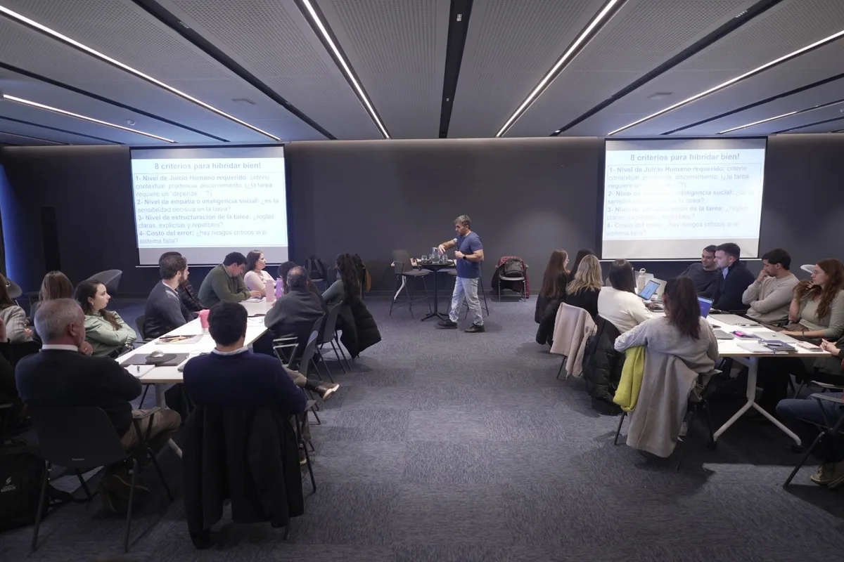 Sala completa durante un taller de rediseño de flujos, con la lámina de los criterios de hibridación proyectada en las dos pantallas